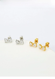 Detail of clover and bow stud earrings in 18k gold and silver with heart zircon inlay