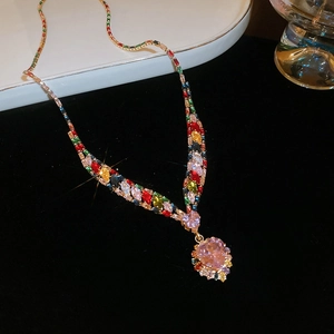 Macro detail of V-shaped gold necklace set with multi-colored gems and heart pendant