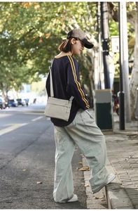 Outdoor view of lightweight beige nylon crossbody bag featuring adjustable strap and zip pocket