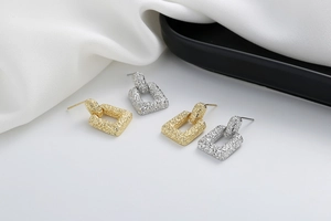 Detail of geometric square earrings featuring vintage hammered textures in gold and silver
