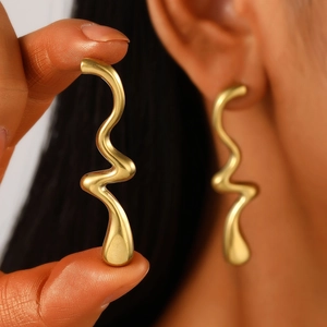 Macro detail of high-polish gold S-shaped wave earring worn to show size and texture