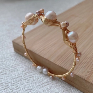 Detail of pink and white pearls hand-wrapped with golden wire on a wooden base