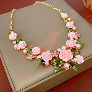 Détail de roses en résine rose et fausses perles sur un collier floral doré