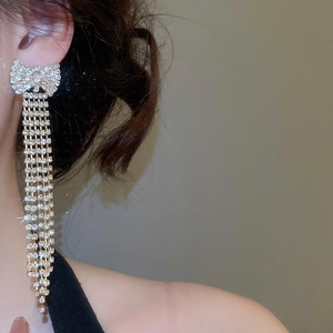 Macro shot of silver bow tassel earrings with sparkling zircons worn by a model
