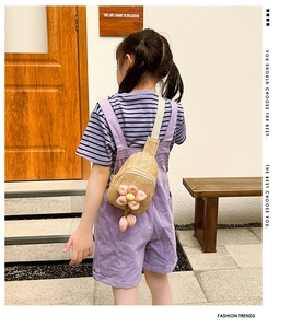 Detail of hand-woven straw crossbody bag with pink plush flowers and tassel for girls