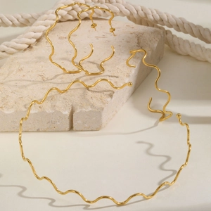 Detail shot of wavy gold necklace and large hoop earrings on a textured stone surface