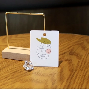 Close-up of a white jewelry display card with minimalist black face line art and green hat
