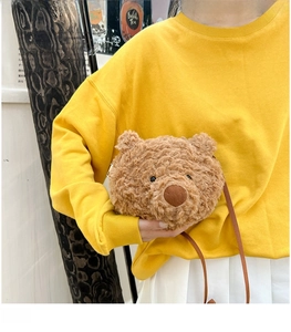 Brown plush bear head crossbody bag worn by model in a stylish outdoor setting