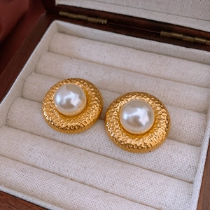 Nahaufnahme von Vintage-Perlenohrsteckern mit gehämmertem Goldboden auf Samtdisplay