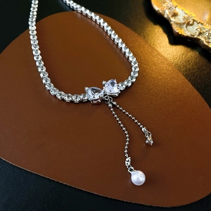 Detail of bow-shaped zircon heart necklace with cascading pearl tassels and silver finish
