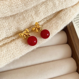 Detailed close-up of red bow and gold sphere earrings on a cream velvet tray