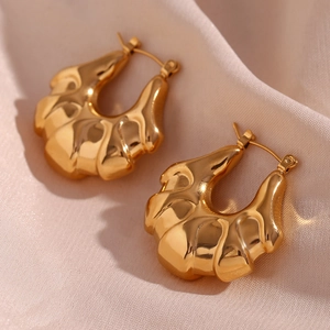 Detailed close-up of gold 18K hollow earrings with irregular wavy texture on pink satin