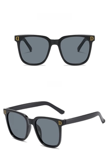 Détail de lunettes de soleil noires avec verres gris et logo D doré sur la branche