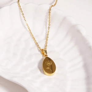 Détail d'un pendentif goutte d'eau dorée avec fleur gravée sur un plateau coquillage