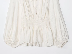 Detail of white lantern sleeve shirt featuring pleated fabric texture and elastic waist