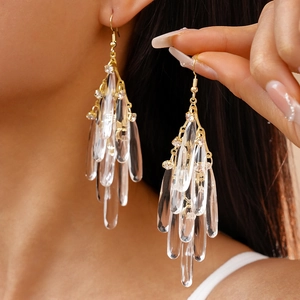 Detail of long gold tassel earrings with clear acrylic teardrop charms on a model