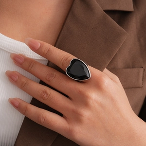 Détail d'une grande bague cœur en pierre noire facettée sur monture argentée au doigt