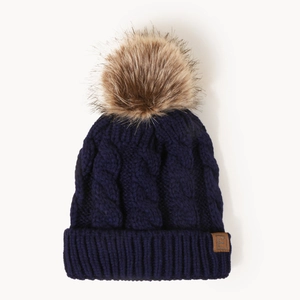 Navy cable knit beanie with faux fur pom pom and leather E logo patch on white background