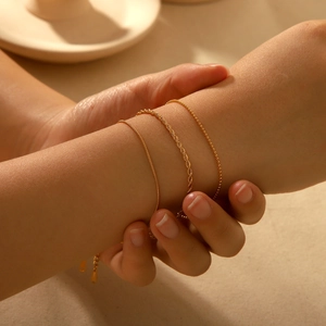 Three-piece set of gold stainless steel snake, twisted, and bead chains on woman's wrist