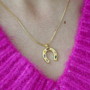 Close-up of golden horseshoe pendant with multi-colored gemstones on a model