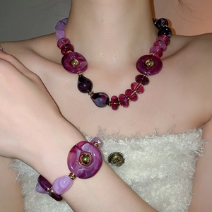Detail view of purple irregular acrylic necklace and bracelet set with golden metal beads
