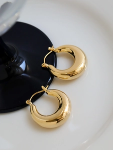 Macro detail of high-polish thick gold C-shaped hoop earrings on a black and white surface