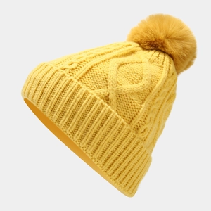 Detailed knit texture of bright yellow winter beanie with soft fluffy faux fur pompom