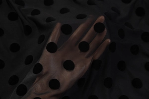 Close-up of black mesh fabric with fuzzy polka dots showing sheer texture and material details
