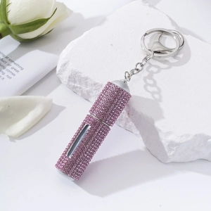 Detail of pink rhinestone portable perfume atomizer keychain on a white marble stone