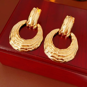 Macro detail of golden hammered texture earrings with wavy design on a wooden surface