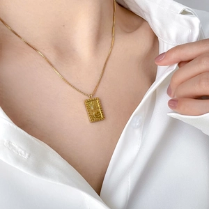 Close-up of a vintage sun rectangular embossed pendant necklace on a gold bead chain