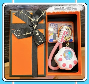Cute pink cat paw keychain with stylish orange gift box featuring black ribbon and gold logo