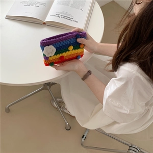 Detailed shot of handmade rainbow crochet bag with white floral accents and colorful pom-poms
