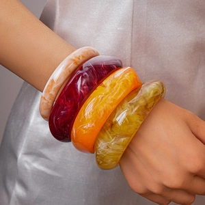 Close-up of four wide resin bangles in marble, amber, and vibrant ink patterns on a model