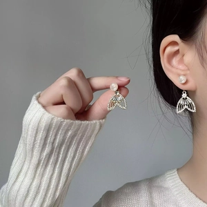 Détail de boucles d'oreilles perle sirène avec strass sur modèle en maille blanche