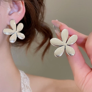 Détail macro de boucles d'oreilles fleur argentées sur modèle et gros plan en main