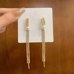 Close-up of gold tassel earrings with sparkling rhinestones and a white imitation pearl