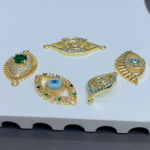 Five gold-plated evil eye charms with colorful crystals on a textured white surface