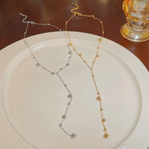 Detail of gold and silver Y-shaped tassel necklaces with polished beads in a ceramic tray