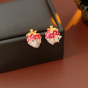 Detailed close-up of gold-plated strawberry earrings with red enamel and white crystals