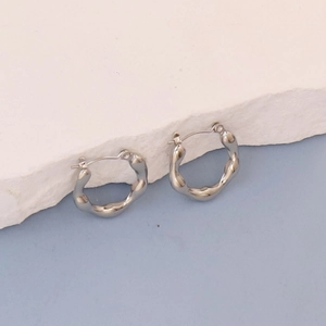 Macro shot of silver textured wavy hoop earrings with polished mirror finish on stone stand
