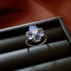 Macro shot of silver floral ring with blue gemstones and twisted band on black leather