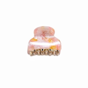 Detailed close-up of a pink and yellow marbled acetate hair claw with gold metal teeth