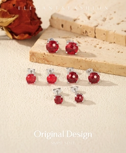Macro shot of red pomegranate zircon earrings in silver settings on a textured surface
