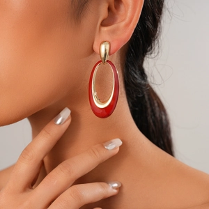 Close-up of a model wearing a gold earring with a large glossy red oval enamel pendant