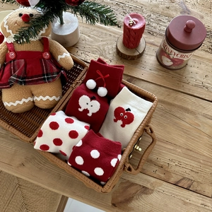 Close-up of thick red Christmas socks with apple patterns and white pom-poms in a basket