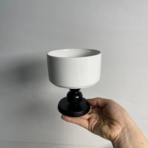 Detail of hand holding a white ceramic bowl with a black wooden stem in a modern setting