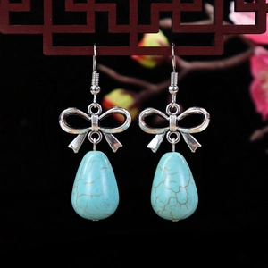 Detail of bohemian drop earrings with silver bow design and turquoise teardrop stones