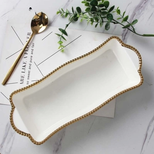 Detail of white ceramic tray with golden beaded rim and handles for dessert or steak