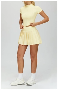 Detail of light yellow yoga set featuring a half-zip short sleeve top and pleated sports skirt